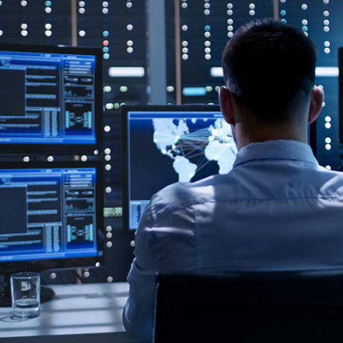 System Security Specialist Working at System Control Center. Roo System Security Specialist Working at System Control Center. Room is Full of Screens Displaying Various Information.